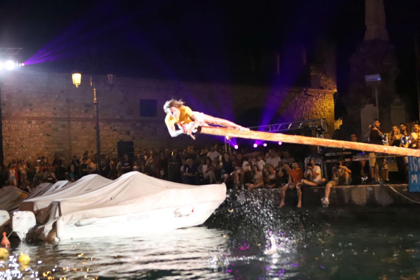 Un concorrente scivola lungo il palo ingrassato tra gli spruzzi d'acqua, di notte, sotto il castello di Lazise